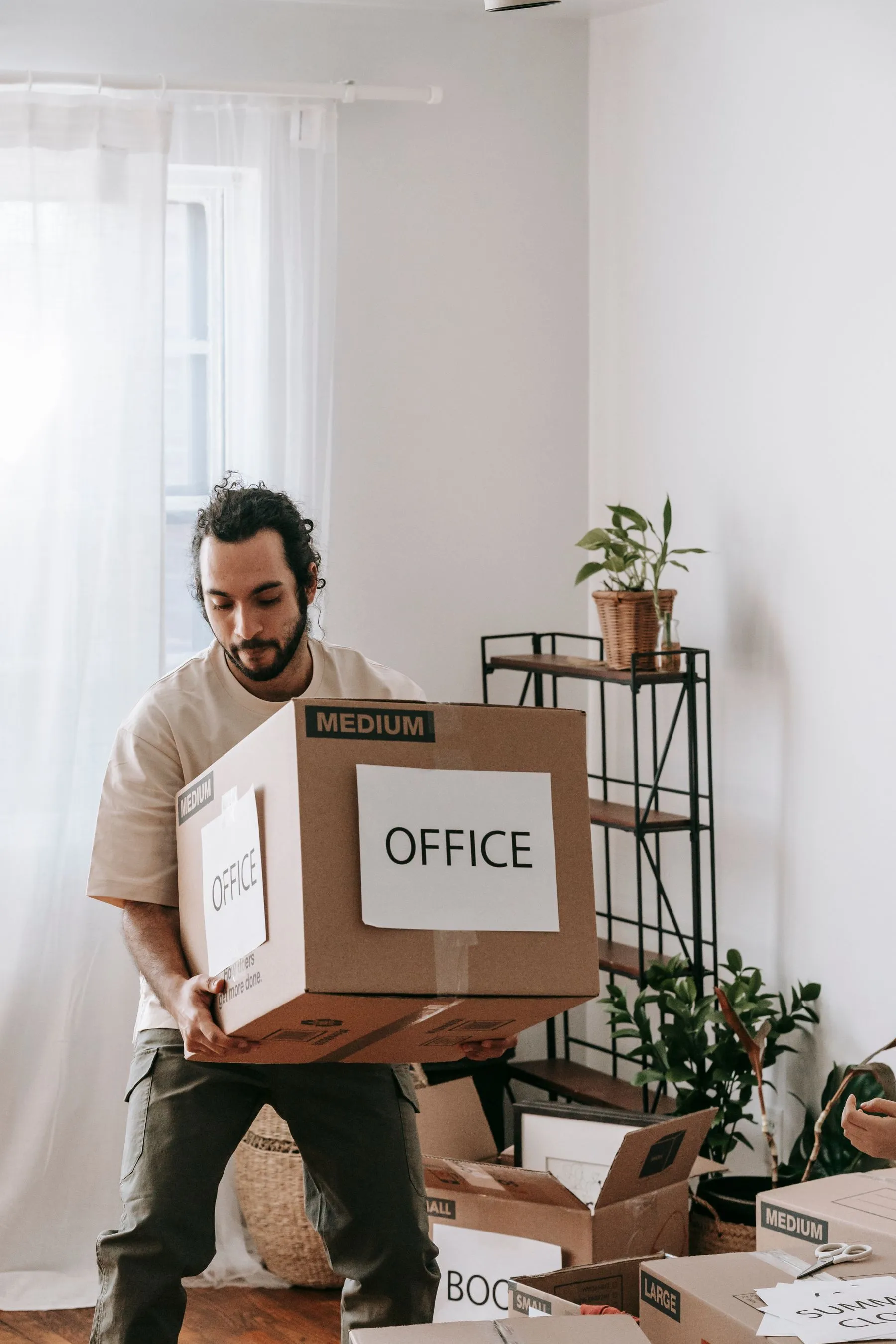 A mover carrying a labelled box through a calm apartment