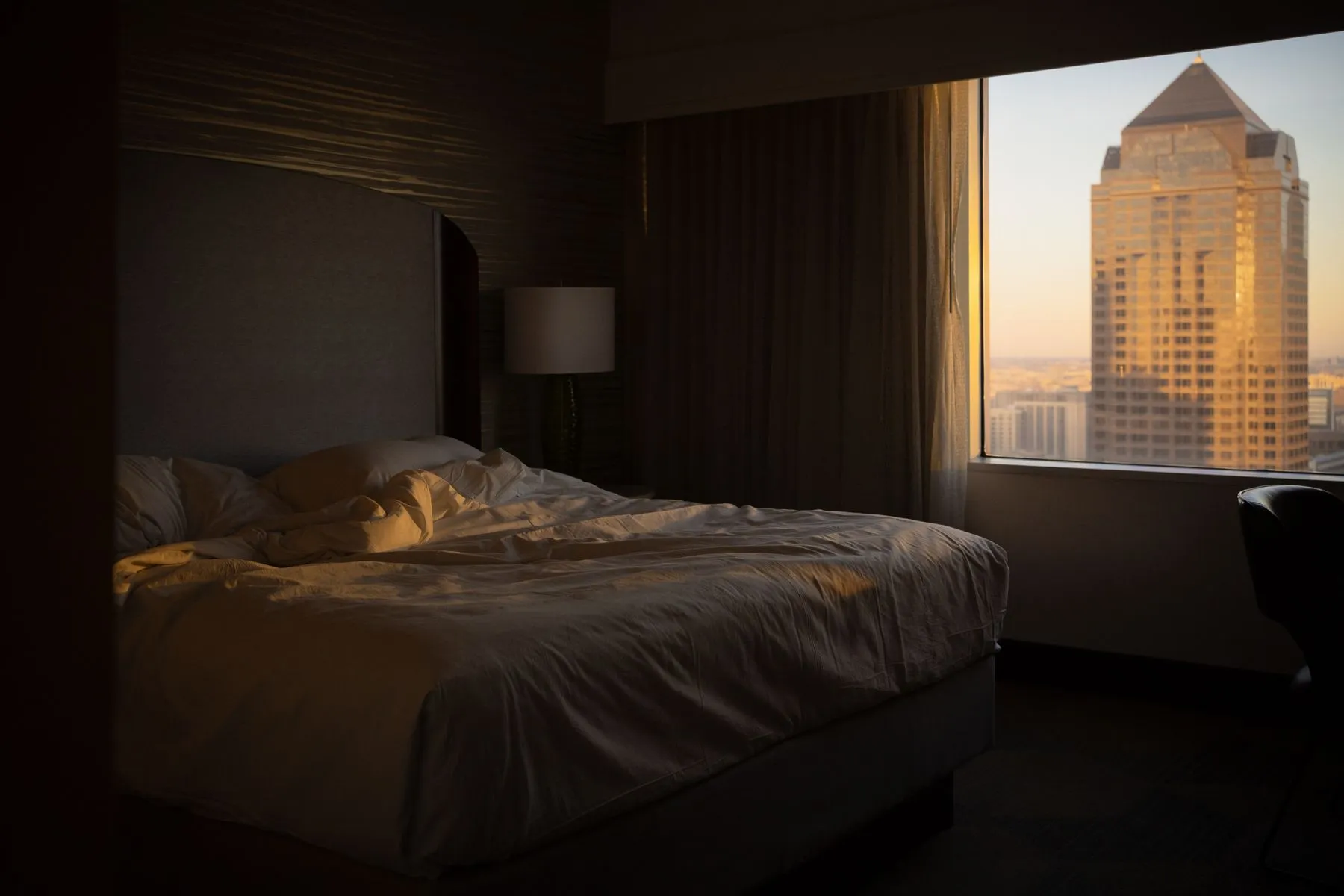 A hotel suite at dusk, a lit lamp and the city skyline beyond