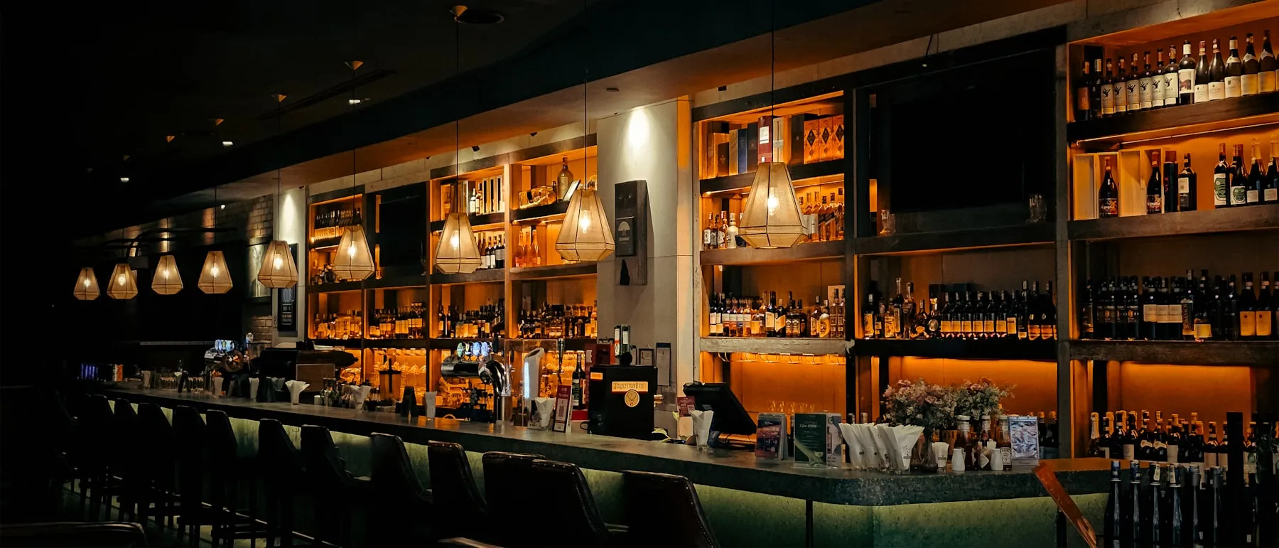 A dimly lit bar with amber-lit bottle shelves